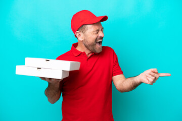 Pizza delivery man with work uniform picking up pizza boxes isolated on blue background pointing...