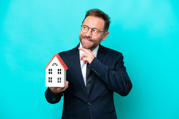 Real estate middle age agent man isolated on blue background looking up while smiling