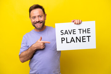 Middle age caucasian man isolated on yellow background holding a placard with text Save the Planet and pointing it