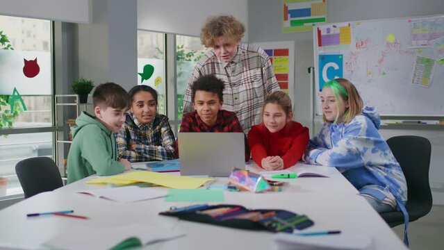 Group of multiethnic teenagers work on project together using computer in classroom