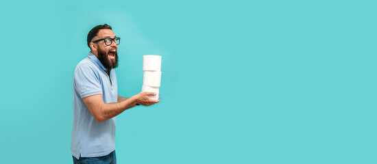 Attractive young caucasian guy holds several rolls of toilet paper in his hands, toilet paper advertisement. Funny promotion poster. Hygiene and sanitation. A man with a joyful face holds toilet paper - obrazy, fototapety, plakaty
