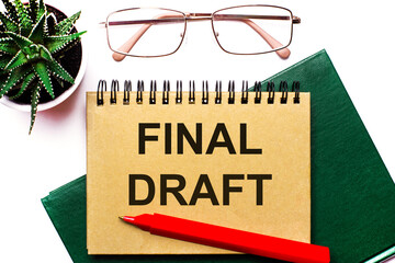On a light background, gold-framed glasses, a flower in a pot, a green notebook, a red pen and a...