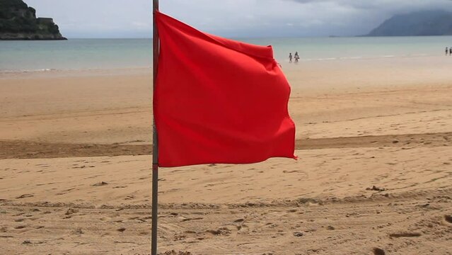 Bandera roja  en playa con gente paseando, Laredo
