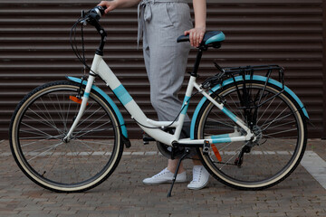 Fototapeta na wymiar White bicycle stands in yard. Behind female legs in trousers