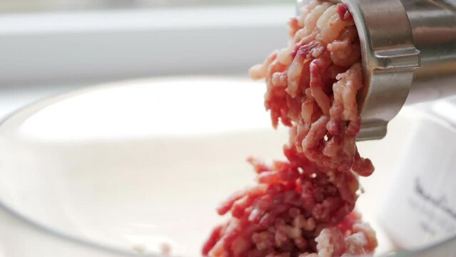 Cooking minced meat with an electric meat grinder in the kitchen. The woman takes pieces of beef meat and puts them in the car. The cook makes blanks for cutlets. Kitchen appliance. Fresh minced meat