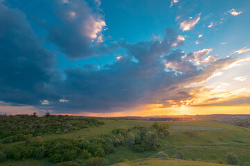 Naklejka na ściany i meble Stunning sunset sky with clouds over green hills. Summer countryside view.