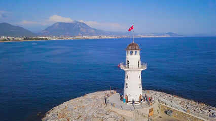 Fototapeta na wymiar Lighthouse on background of seascape and coastal city. Clip. Top view of beautiful seascape with white lighthouse off coast of resort town