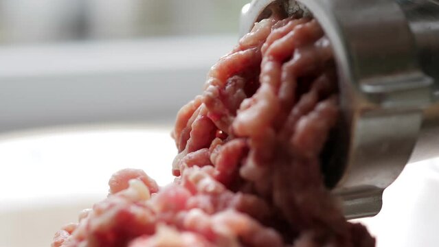 Cooking minced meat with an electric meat grinder in the kitchen. The woman takes pieces of beef meat and puts them in the car. The cook makes blanks for cutlets. Kitchen appliance. Fresh minced meat