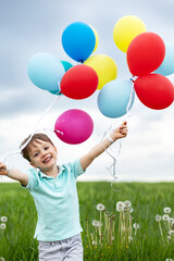 four-year-old boy with balloons walks in a green meadow with dandelions