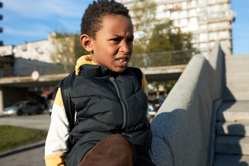 Cool 9-years-old African American male kid sitting on railing of concrete stairs outdoors against...