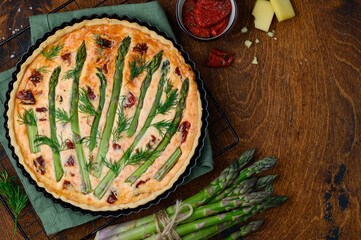Quiche or tart with asparagus and sun-dried tomatoes in form on a wooden table. Top view - obrazy, fototapety, plakaty