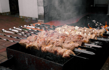 Marinated meat with onion, food cooking on skewers on fire. Preparing pork shashlik on a charcoal mangal. Beef grill. BBQ. Side view. Outdoors picnic. Traditional tasty shish. Juicy meal. Close-up