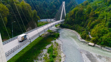 Fototapeta na wymiar Truck crosses beautiful bridge in summer. Scene. Top view of truck carrying things driving across bridge on background of beautiful forest landscape. Travel and relocation