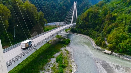 Fototapeten Truck crosses beautiful bridge in summer. Scene. Top view of truck carrying things driving across bridge on background of beautiful forest landscape. Travel and relocation © Media Whale Stock