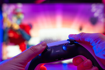 Close-up. Joystick in the hands of a gamer on a multi-colored background. Video games, modern equipment, electronics, computer equipment, hobbies, fun pastime.