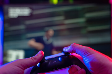 Modern joystick in the hands of a gamer. A gamer plays video games online with friends on a large TV screen. New technologies, modern digital equipment, youth culture.