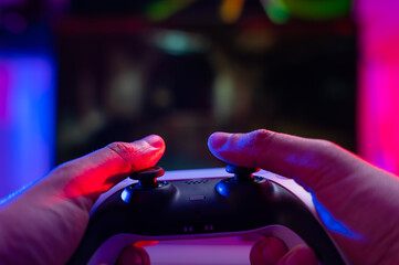 Close-up. Joystick in the hands of a gamer on a dark background. Neon lighting. Video games on modern digital equipment. Cyberspace, cybersport, virtual reality.