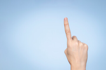 Hand gesture. Female hand shows number one. Woman pointing up with index finger on light blue background