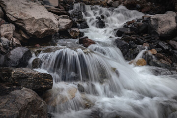 Close-up shot of a mountain stream with a waterfall runs over the stones between the rocky banks