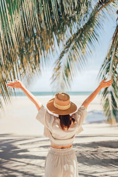 Summer beach vacation concept, Happy woman with hat relaxing at the seaside and looking away, in the summer against a backdrop of palm trees and sea beach.