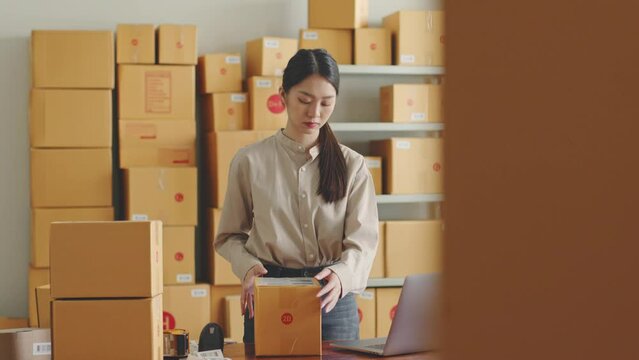 Asian woman working at online store warehouse, using barcode reader check on customer parcel box, online e-commerce retail small business concept