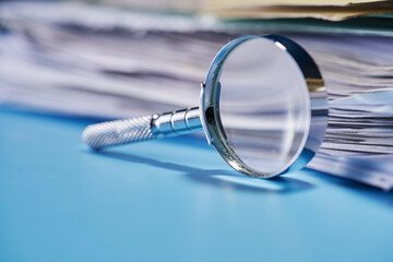 selective focus magnifying glass leans against a thick stack of documents.