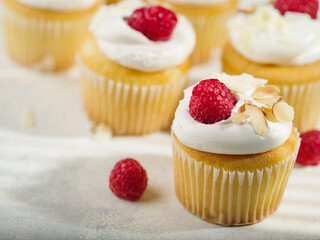 Lots of muffins with cream, raspberries and almond pieces. Isolated on white background. Festive composition. Restaurant, hotel, cafe, confectionery, home cooking.