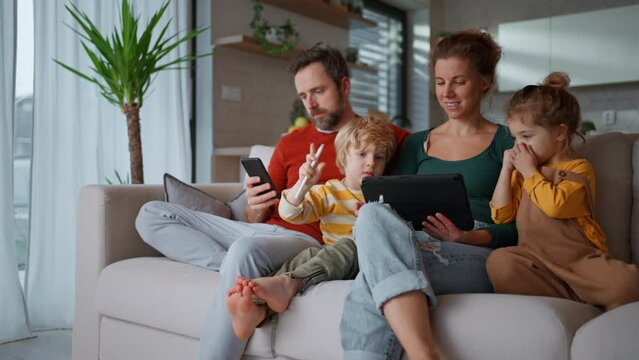 Little children sitting with parents on sofa and using tablet at home