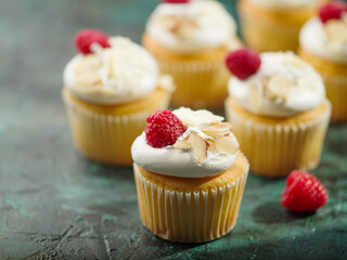 Lots of delicious muffins with whipped cream, fresh raspberries, garnished with walnut pieces. Dark green marble background. Cafe, confectionery, restaurant, hotel, home cooking.