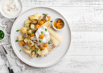Fried cod fillet served with baked potato and grilled mushrooms, yellow berries and cloudberry sauce. Delicious food. Hot dinner or lunch. White background.