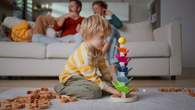 Little boy playing with wodden toys at home, heis parents at background
