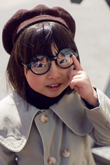 Korean girl in a gray coat and cap and round glasses stands the street in spring