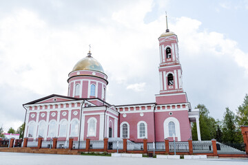 Fototapeta na wymiar Orthodox church in the city of Birsk Russia Bashkortostan, a place of pilgrimage for Christians, a bell tower with a peak on the roof, a pink building.