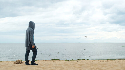 Side view of a man looking at the river and birds flying in the sky. Concept. Male standing on sandy lake shore, looking into the distance at soaring seagulls.