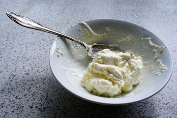 Weiße Keramikschüssel mit weißer Sahne und silbernem Löffel auf weißem Tisch 