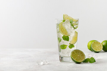 Glass of cold mojito, lemonade with ice, lime and mint on grey background, fresh summer tonic. Cold drink. Copy space