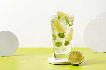 Mojito, Iced cold summer drink. Glass of cold tonic with lime on podium. Lemonade drink with ice and mint on green background.
