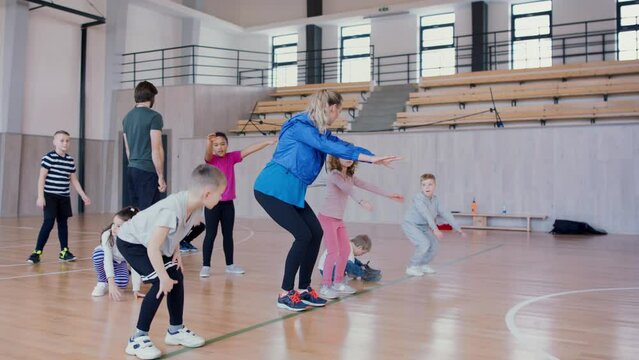 PE teachers and group of elementary students exercising during class at school gym.
