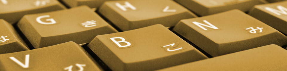 Japanese typing. Dark yellow laptop keyboard closeup. Symbols on buttons of hiragana. Light brown...