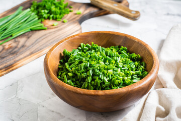 Fresh chopped green onions in a wooden bowl and a cutting board on the table.  Close-up