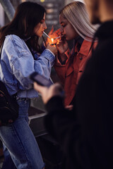 Fototapeta na wymiar Two rebellious teenage girls lightning cigarettes and smoke. Teenagers smoking cigarettes