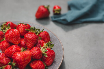 Delicious, fresh strawberries in a stylish plate on a concrete background. Top view with space to copy.