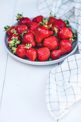 Delicious, fresh strawberries in a stylish plate on a white wooden background. Top view with space to copy.