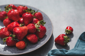 Delicious, fresh strawberries in a stylish plate on a concrete background. Top view with space to copy.
