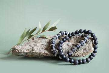 Two bracelets made of natural black volcanic lava stones beads isolated on pastel greenbackground. Handmade jewelry. Woman exoteric accessories. Talismans and amulets. Selective focus - obrazy, fototapety, plakaty