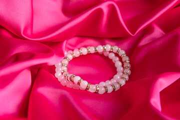 Two bracelets made of natural pink quartz stones beads on crimson silk fabric background. Handmade jewelry. Woman exoteric accessories. Talismans and amulets. Selective focus