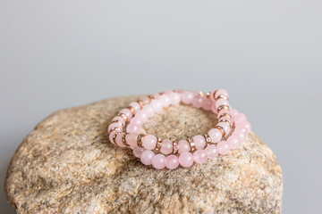 Two bracelets made of natural pink quartz stones beads isolated on pastel beige background. Handmade jewelry. Woman exoteric accessories. Talismans and amulets. Selective focus - obrazy, fototapety, plakaty