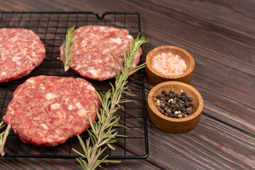 Homemade minced pork and beef patties, with spices, rosemary, ready for roasting, for cooking burgers on a grill, on a wooden background