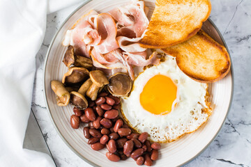Traditional English breakfast with egg, bacon, beans, mushrooms and toast on a plate. Top view