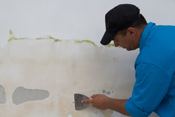 Image of a laborer who with a spatula removes plaster and mold from a wall to be restored